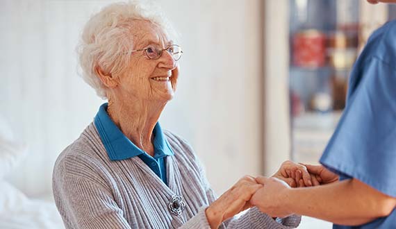 Nurse giving a friendly, helping hand to smiling senior woman
