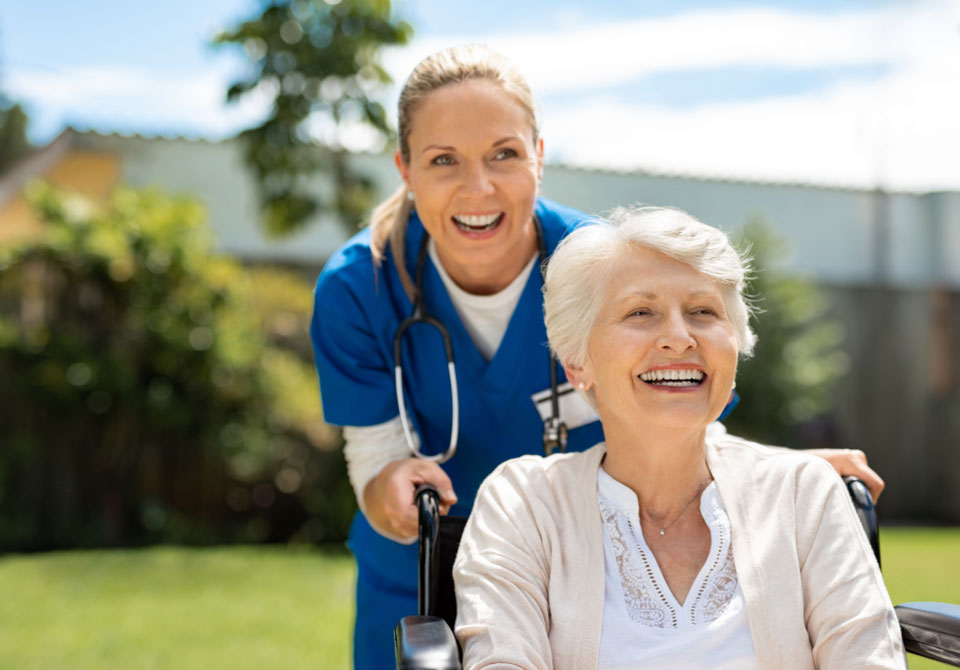 nurse laughing with senior woman in wheelchair